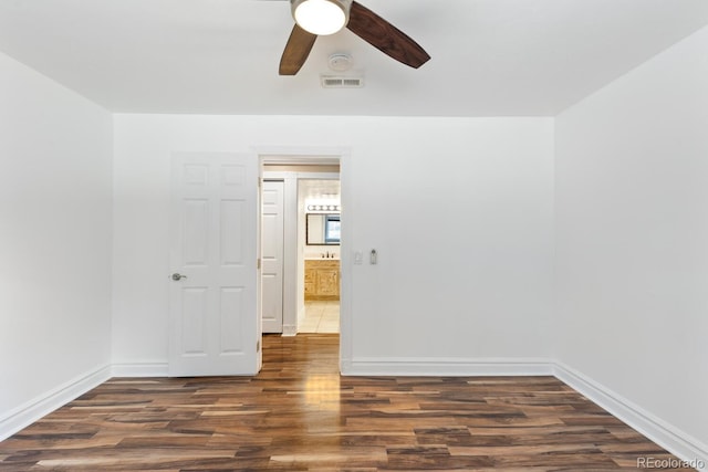 empty room featuring ceiling fan, dark wood-style flooring, visible vents, and baseboards