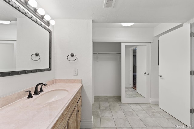 bathroom with a textured ceiling, vanity, visible vents, a spacious closet, and tile patterned floors