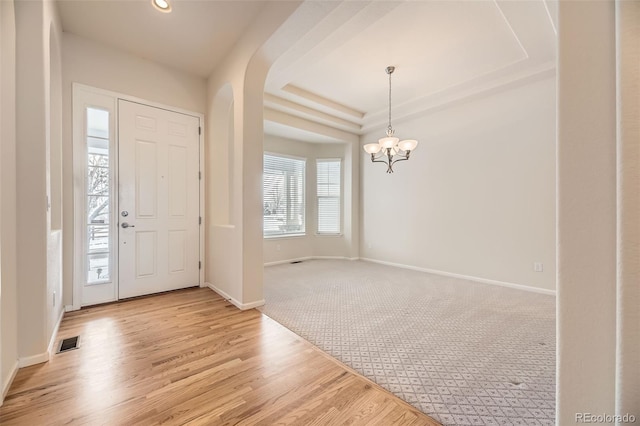 carpeted foyer featuring a notable chandelier and a raised ceiling