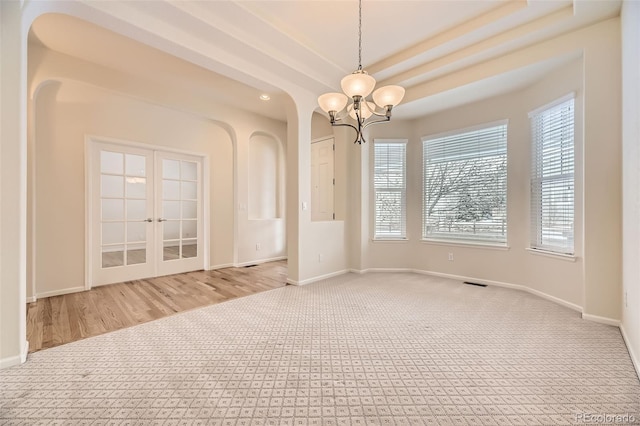 carpeted empty room with a raised ceiling and a chandelier