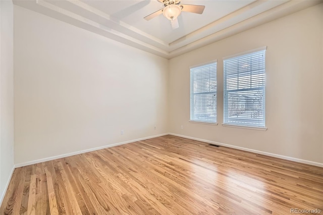 empty room featuring a tray ceiling, ceiling fan, and light hardwood / wood-style floors