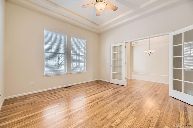 spare room featuring french doors, ceiling fan with notable chandelier, a raised ceiling, and hardwood / wood-style floors