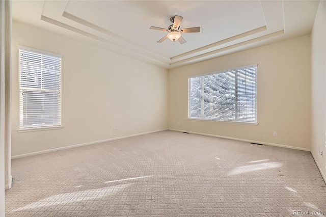 empty room featuring ceiling fan, a healthy amount of sunlight, light carpet, and a tray ceiling