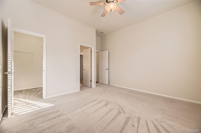 unfurnished bedroom with light carpet, a walk in closet, a closet, and ceiling fan