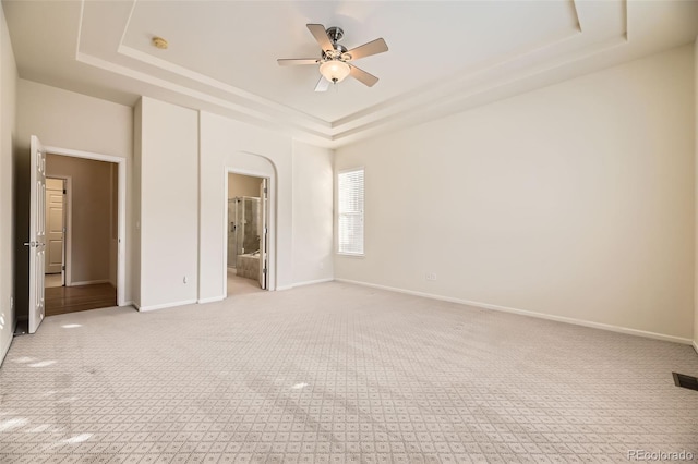 unfurnished bedroom featuring a tray ceiling, ensuite bathroom, ceiling fan, and light carpet