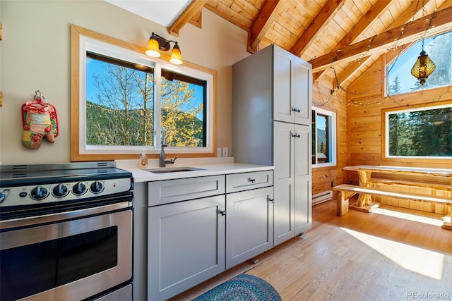 kitchen featuring sink, wooden walls, gray cabinets, stainless steel range oven, and light hardwood / wood-style floors