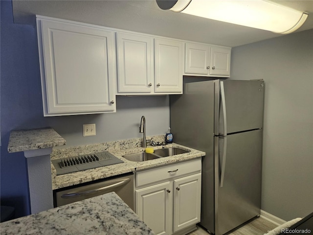 kitchen featuring light stone counters, appliances with stainless steel finishes, white cabinets, a sink, and baseboards