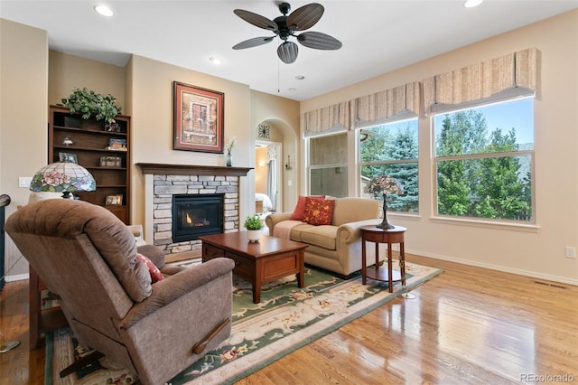 living room featuring a stone fireplace, ceiling fan, and light wood-type flooring