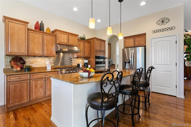 kitchen featuring sink, appliances with stainless steel finishes, a kitchen island with sink, stone countertops, and decorative light fixtures