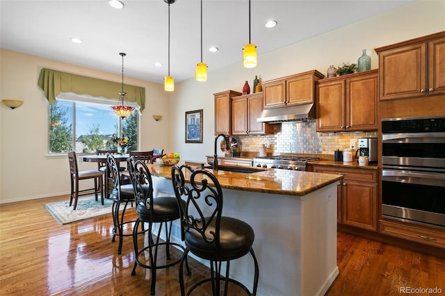 kitchen featuring pendant lighting, a kitchen breakfast bar, stove, a kitchen island with sink, and stainless steel double oven