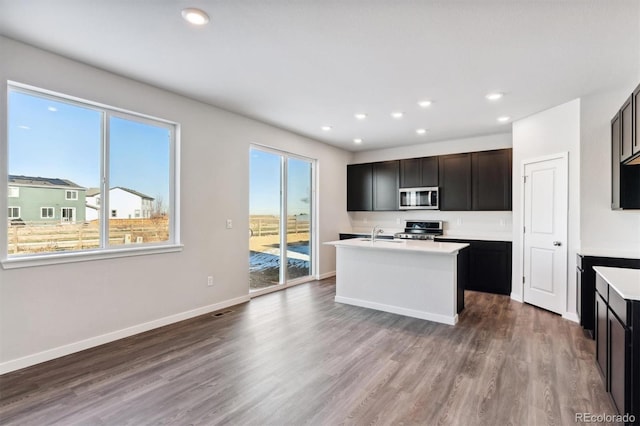 kitchen with a kitchen island with sink, appliances with stainless steel finishes, light countertops, and wood finished floors