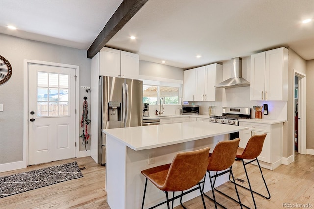 2337 S Franklin St, Denver, CO 80210 - kitchen featuring wall chimney range hood, stainless steel appliances, light wood-style flooring, white cabinets, and beamed ceiling