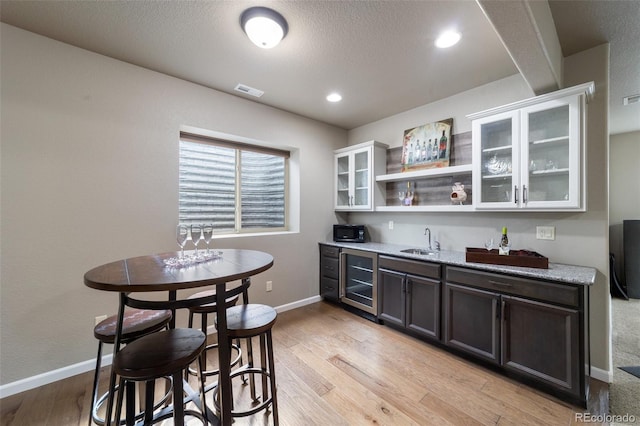 dining room featuring wet bar, a textured ceiling, wine cooler, and light hardwood / wood-style floors