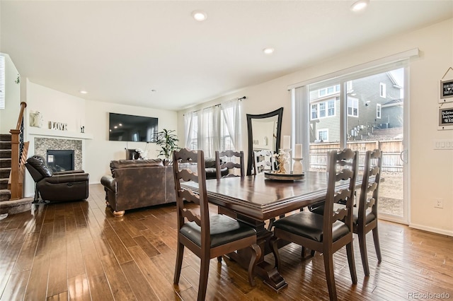 dining room featuring recessed lighting, dark wood-type flooring, baseboards, stairs, and a glass covered fireplace