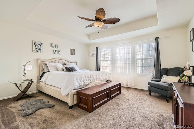 carpeted bedroom featuring a raised ceiling, ceiling fan, and baseboards