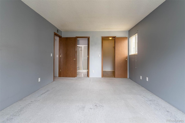 unfurnished bedroom with ensuite bath, a textured ceiling, and carpet