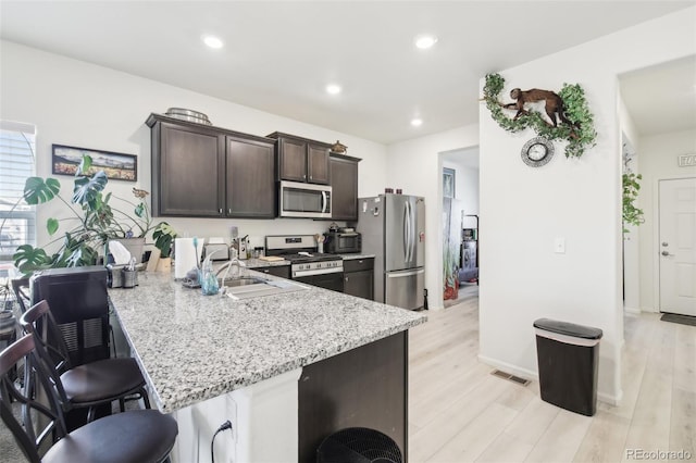 310 Quincy Rr Ave, Keenesburg, CO 80643 - kitchen featuring light stone counters, a kitchen breakfast bar, dark brown cabinetry, stainless steel appliances, and light wood-style flooring