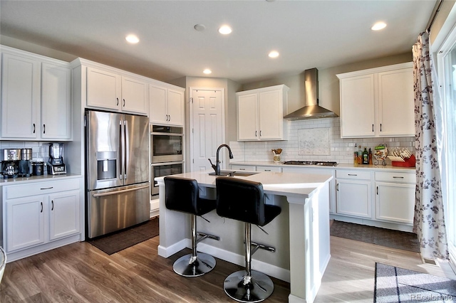 kitchen with white cabinets, a sink, wall chimney exhaust hood, stainless steel appliances, and wood finished floors
