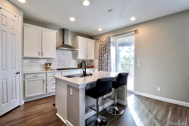 kitchen featuring wall chimney range hood, white cabinets, dark wood-style flooring, a sink, and backsplash
