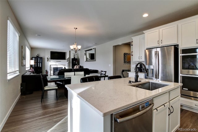 kitchen with an island with sink, dark wood-type flooring, white cabinets, a sink, and appliances with stainless steel finishes