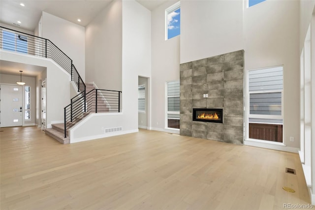 unfurnished living room with a tiled fireplace, a towering ceiling, and light hardwood / wood-style floors