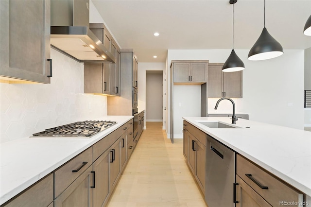 kitchen with sink, wall chimney exhaust hood, hanging light fixtures, decorative backsplash, and appliances with stainless steel finishes