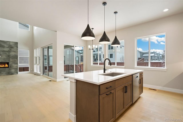 kitchen with a fireplace, a kitchen island with sink, sink, and light wood-type flooring