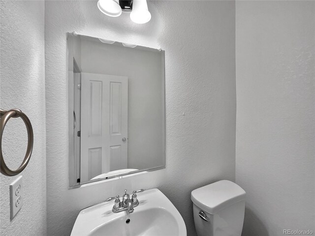 half bath with toilet, a textured wall, and a sink