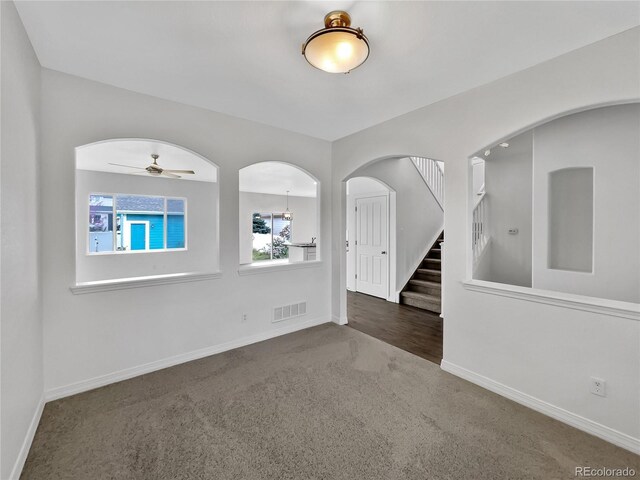 carpeted empty room with arched walkways, a ceiling fan, baseboards, visible vents, and stairway