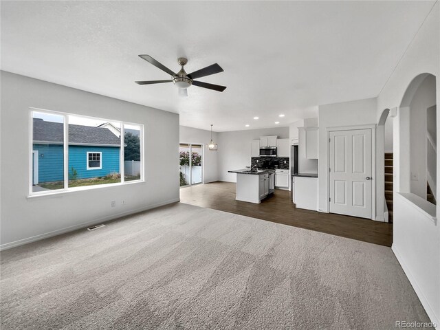 unfurnished living room featuring arched walkways, ceiling fan, baseboards, and dark colored carpet