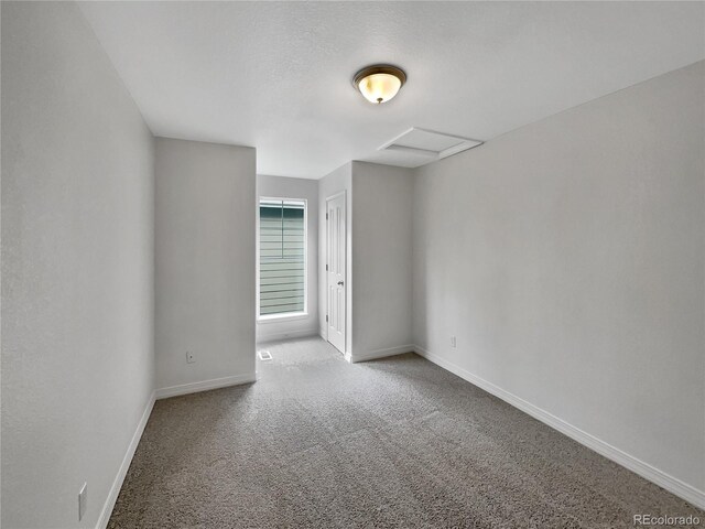 unfurnished room with carpet floors, baseboards, and attic access