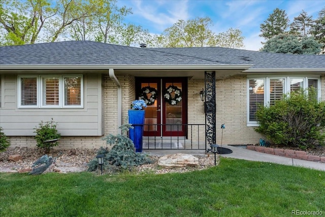 view of front of house with a shingled roof, a front yard, and brick siding