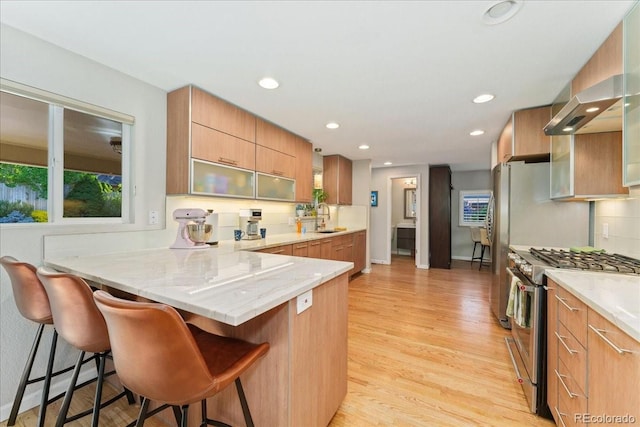 kitchen featuring light wood-style flooring, stainless steel range with gas stovetop, a sink, a peninsula, and a kitchen bar