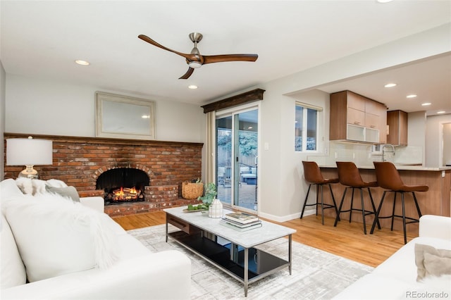 living area with light wood-style flooring, a fireplace, ceiling fan, and recessed lighting