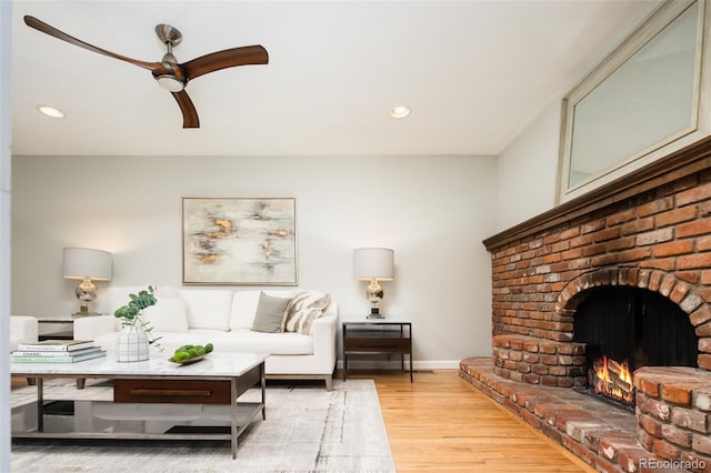 living area with baseboards, recessed lighting, a brick fireplace, and light wood-style floors