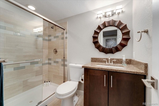 bathroom featuring a textured wall, toilet, a textured ceiling, vanity, and a shower stall