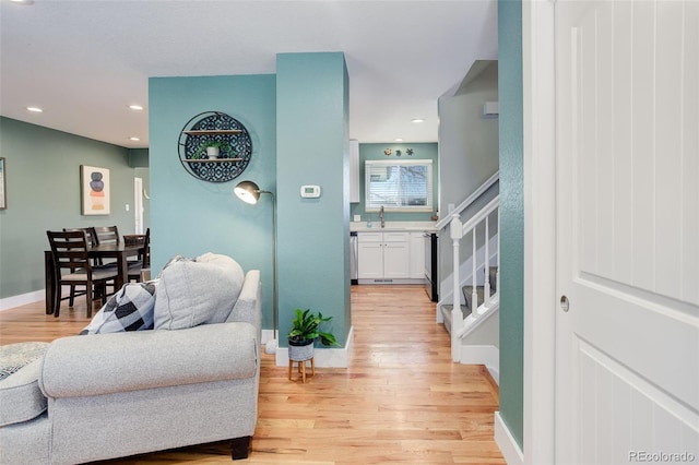 hall featuring a sink, light wood-style floors, recessed lighting, baseboards, and stairway