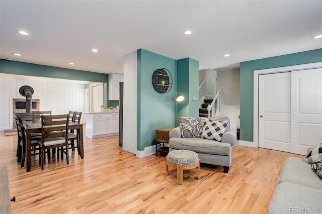 living room featuring a wood stove, stairs, recessed lighting, baseboards, and light wood-type flooring