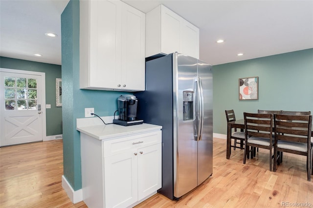 kitchen featuring stainless steel refrigerator with ice dispenser, light countertops, baseboards, white cabinets, and light wood-style floors