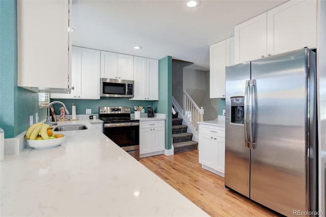kitchen with appliances with stainless steel finishes, light stone countertops, a sink, recessed lighting, and white cabinetry