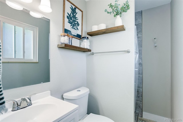bathroom with toilet, a tile shower, and vanity