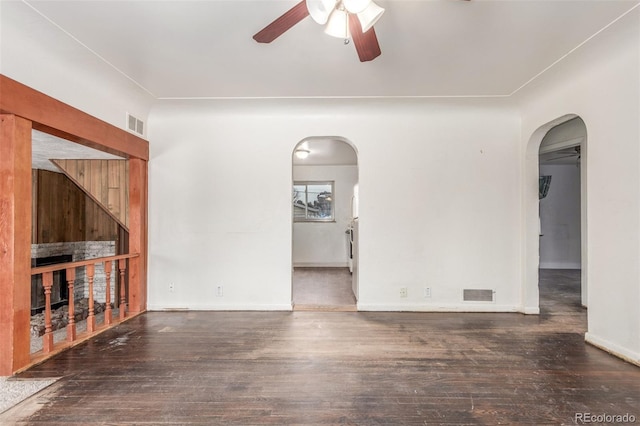 unfurnished living room featuring arched walkways, dark wood finished floors, visible vents, ceiling fan, and baseboards