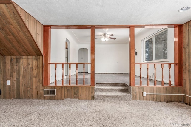 carpeted empty room featuring a textured ceiling, a ceiling fan, and wooden walls