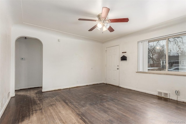 empty room with ceiling fan, visible vents, arched walkways, and dark wood-type flooring