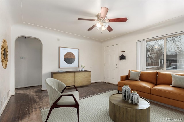 living area featuring arched walkways, dark wood finished floors, baseboards, and ceiling fan