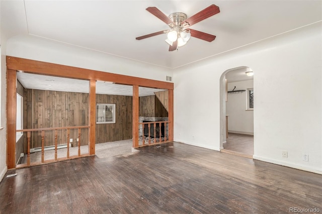 spare room featuring a baseboard radiator, wood walls, dark wood-style flooring, visible vents, and a ceiling fan