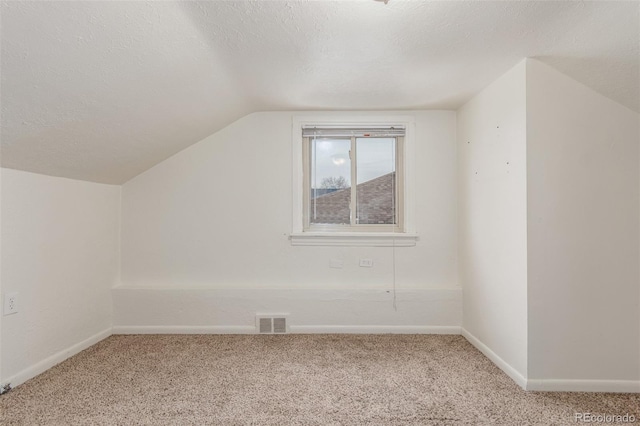 additional living space featuring visible vents, vaulted ceiling, a textured ceiling, and carpet flooring