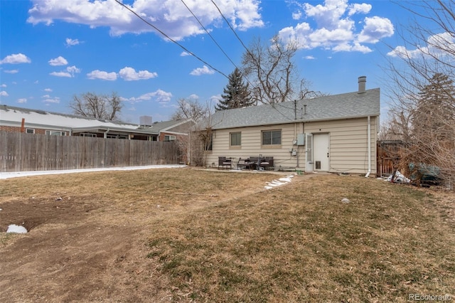 back of property with a shingled roof, a lawn, and fence