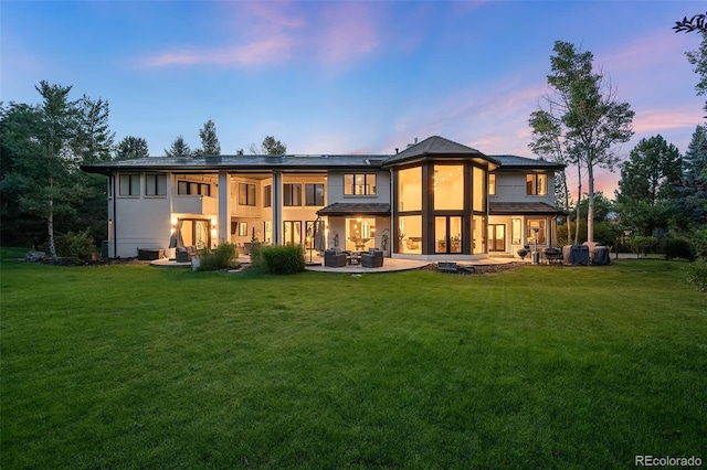 back house at dusk with a lawn and a patio area