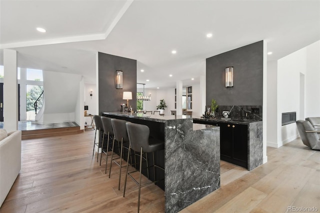 bar featuring dark stone countertops, a fireplace, light hardwood / wood-style flooring, and sink